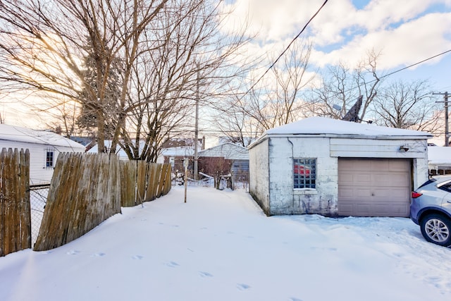 yard layered in snow with an outbuilding, fence, and a garage