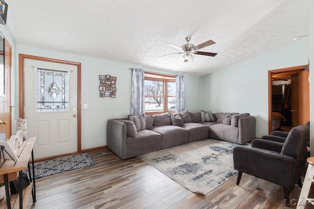 living area with a ceiling fan, vaulted ceiling, a textured ceiling, wood finished floors, and baseboards