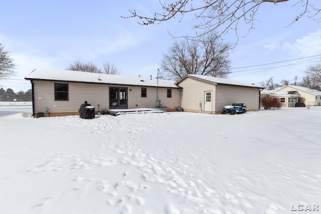 snow covered rear of property featuring a detached garage