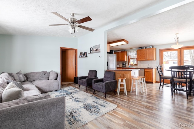 living area with lofted ceiling, light wood finished floors, a ceiling fan, and a textured ceiling