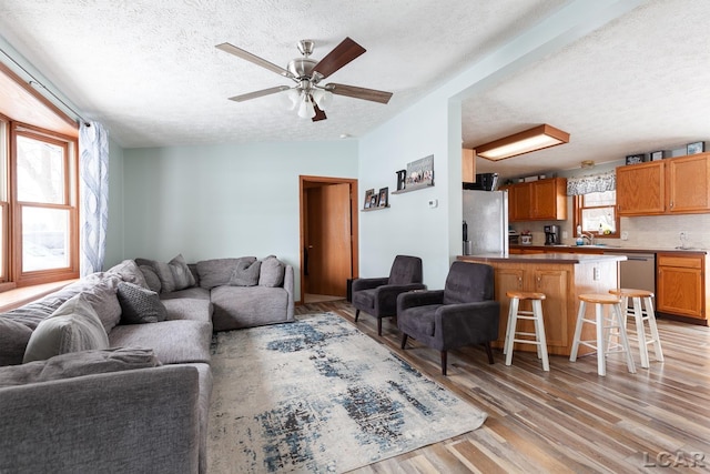 living room with lofted ceiling, ceiling fan, light wood finished floors, and a textured ceiling