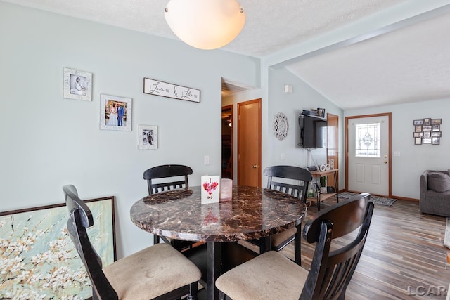 dining area with vaulted ceiling with beams, a textured ceiling, wood finished floors, and baseboards