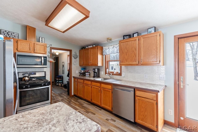 kitchen featuring stainless steel appliances, lofted ceiling, tasteful backsplash, light countertops, and a sink