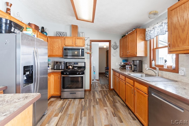 kitchen featuring a sink, vaulted ceiling, light countertops, appliances with stainless steel finishes, and light wood finished floors