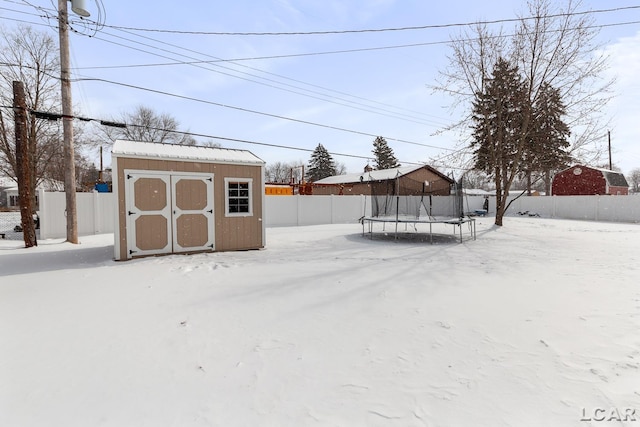 yard covered in snow featuring a trampoline, fence, an outdoor structure, and a shed