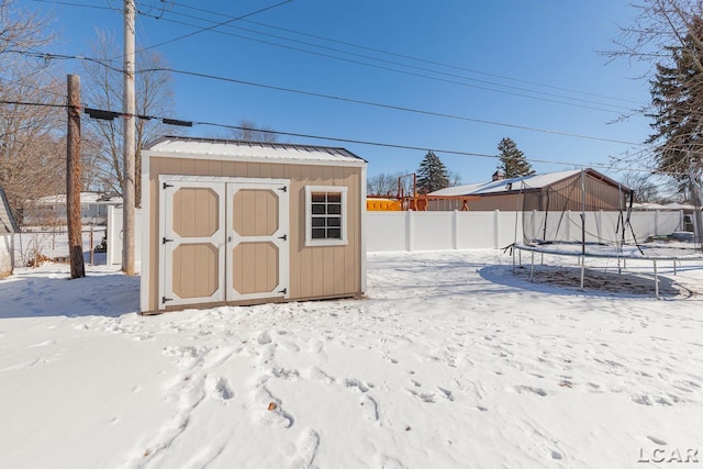 snow covered structure with a storage shed, a trampoline, an outbuilding, and a fenced backyard