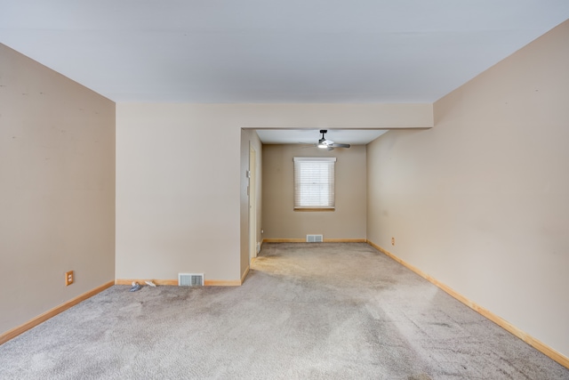 empty room featuring light carpet, ceiling fan, visible vents, and baseboards