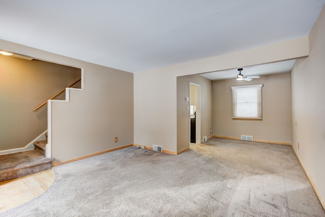 carpeted spare room featuring a ceiling fan, stairway, visible vents, and baseboards