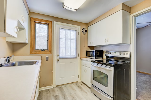 kitchen featuring light wood finished floors, white cabinets, stainless steel appliances, light countertops, and a sink