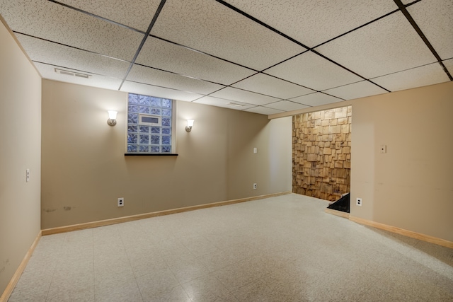 finished below grade area with a paneled ceiling, baseboards, visible vents, and tile patterned floors