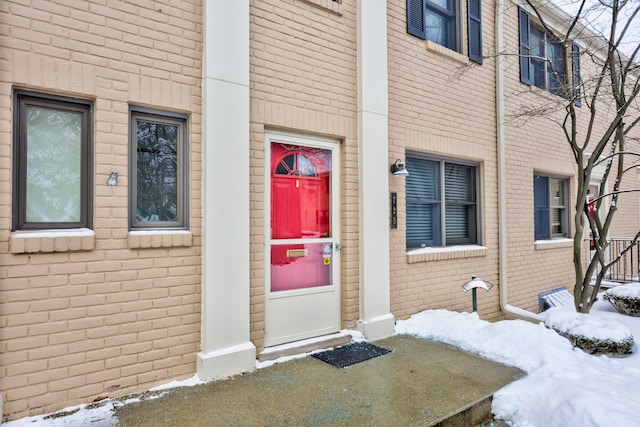 snow covered property entrance with brick siding