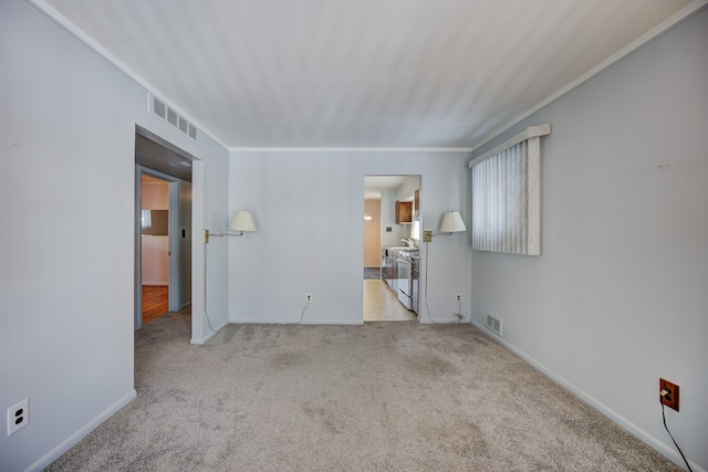 spare room featuring baseboards, ornamental molding, visible vents, and light colored carpet