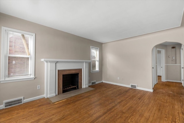 unfurnished living room with arched walkways, wood finished floors, and visible vents