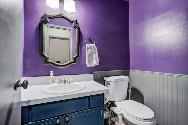 half bathroom featuring a wainscoted wall, vanity, and toilet