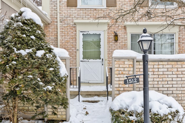 snow covered property entrance with brick siding