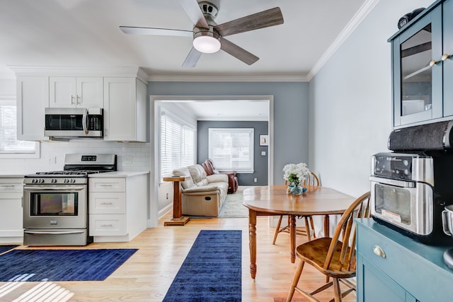 kitchen featuring light wood finished floors, stainless steel appliances, light countertops, ornamental molding, and white cabinets