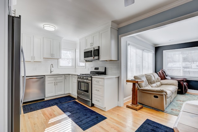 kitchen with white cabinetry, open floor plan, light countertops, appliances with stainless steel finishes, and crown molding