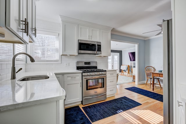 kitchen with a sink, stainless steel appliances, crown molding, white cabinetry, and backsplash