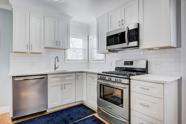 kitchen featuring a sink, white cabinetry, light countertops, appliances with stainless steel finishes, and crown molding