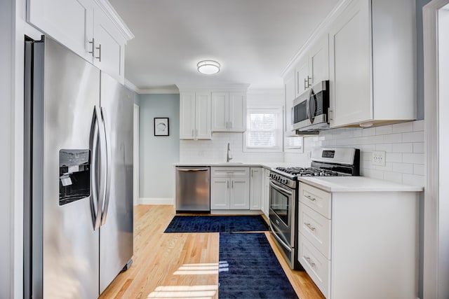 kitchen featuring stainless steel appliances, a sink, white cabinetry, light countertops, and ornamental molding