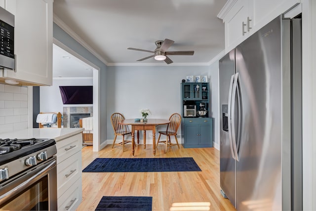 kitchen with crown molding, light wood finished floors, light countertops, appliances with stainless steel finishes, and white cabinetry