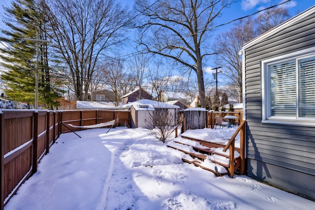 yard covered in snow featuring a fenced backyard, an outdoor structure, a deck, and a storage shed