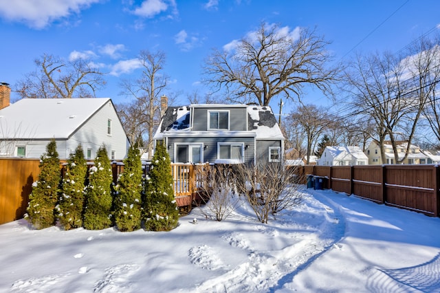 snow covered rear of property featuring a chimney and fence private yard