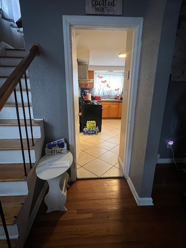 corridor featuring stairs, a textured wall, wood finished floors, and baseboards