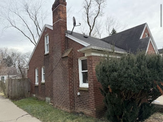 view of side of home featuring brick siding, a chimney, and fence