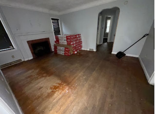 living area with dark wood-style floors, arched walkways, a brick fireplace, and baseboards