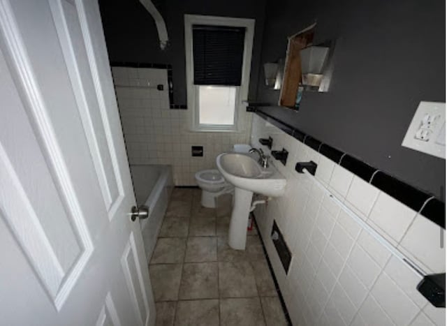 bathroom featuring tile patterned flooring, toilet, a sink, tile walls, and a tub