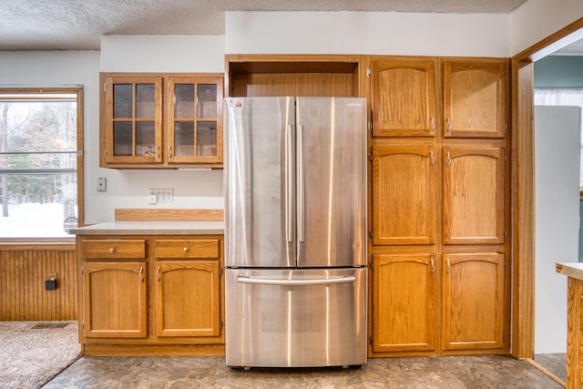 kitchen with glass insert cabinets, freestanding refrigerator, brown cabinetry, and light countertops