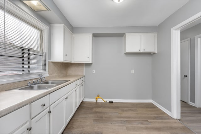 kitchen with light countertops, a sink, white cabinetry, and baseboards