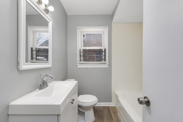 full bathroom with toilet, a bathing tub, wood finished floors, vanity, and baseboards