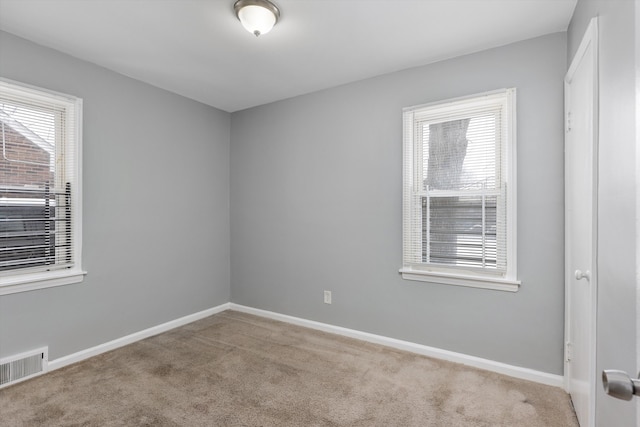 spare room featuring plenty of natural light, visible vents, baseboards, and light colored carpet