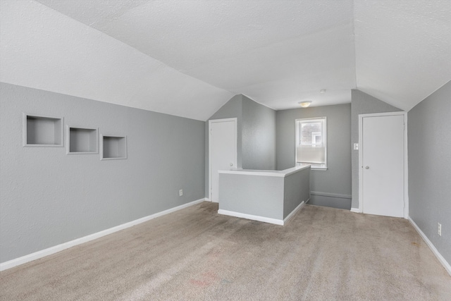 bonus room featuring vaulted ceiling, a textured ceiling, light colored carpet, and baseboards