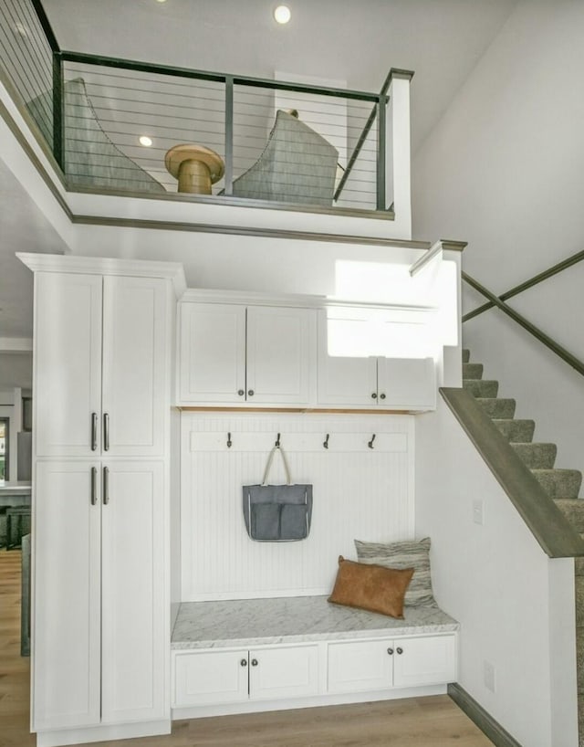 mudroom featuring light wood-type flooring, a towering ceiling, and baseboards