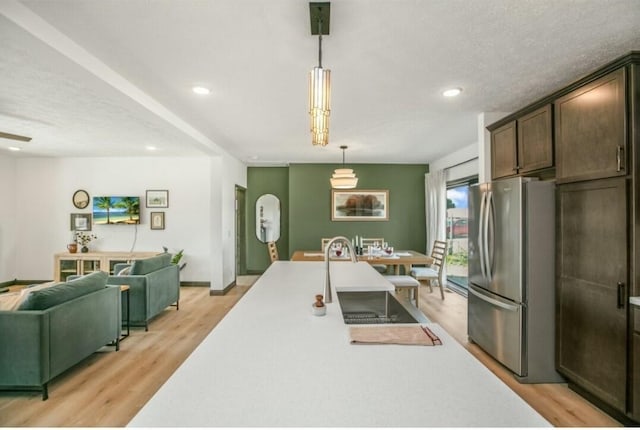 kitchen with pendant lighting, light countertops, freestanding refrigerator, open floor plan, and dark brown cabinetry