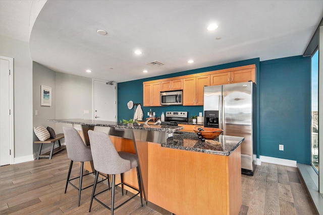 kitchen featuring visible vents, appliances with stainless steel finishes, wood finished floors, and a kitchen island with sink