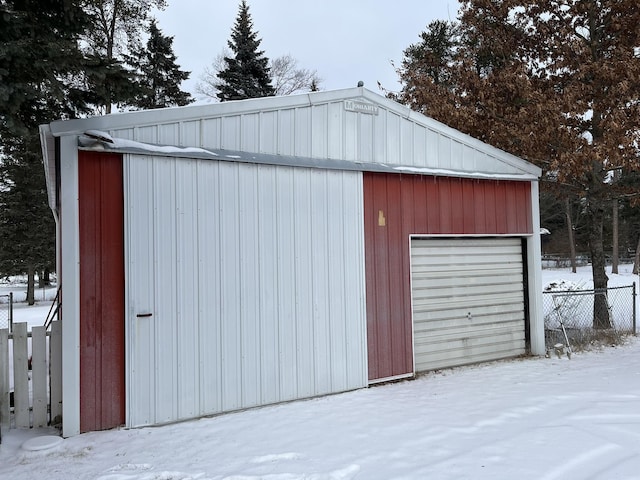 snow covered structure featuring an outbuilding and fence