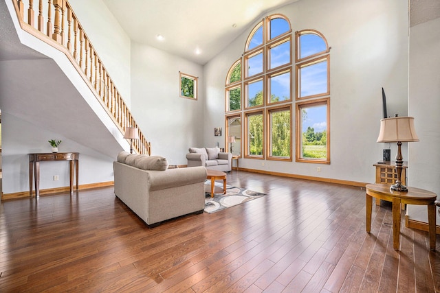 living area with high vaulted ceiling, baseboards, stairway, and hardwood / wood-style floors