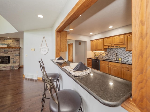 kitchen featuring dishwasher, dark countertops, a breakfast bar area, dark wood-style flooring, and a sink