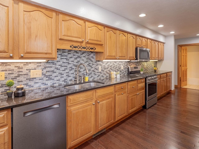 kitchen with tasteful backsplash, appliances with stainless steel finishes, dark wood-type flooring, a sink, and dark stone counters