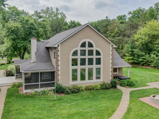 exterior space with a sunroom, a shingled roof, a chimney, and a yard