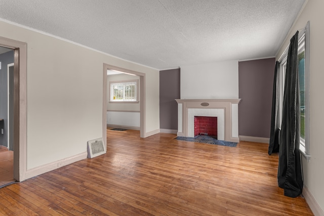 unfurnished living room with light wood finished floors, baseboards, visible vents, a tile fireplace, and a textured ceiling