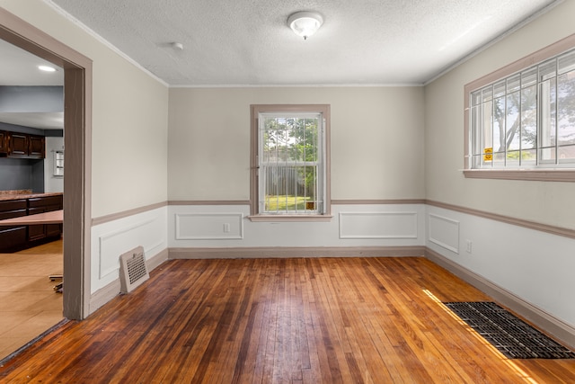 empty room featuring a textured ceiling, wainscoting, wood finished floors, and visible vents