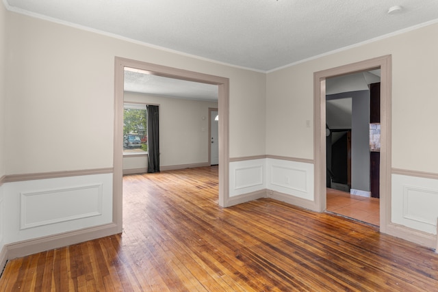 spare room featuring a textured ceiling, a wainscoted wall, wood finished floors, and crown molding