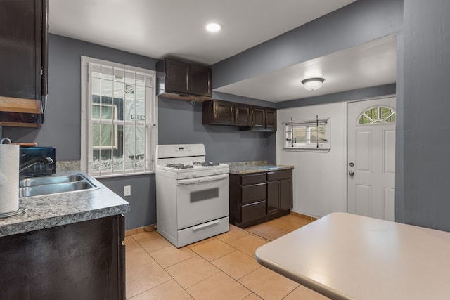 kitchen with light tile patterned flooring, white range with gas stovetop, a sink, dark brown cabinets, and light countertops