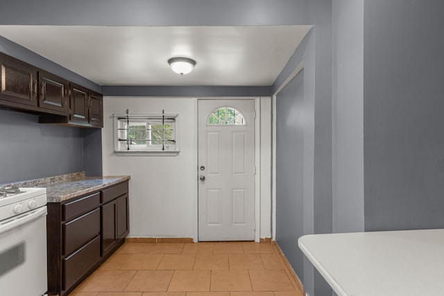 kitchen with light tile patterned floors, white gas range, baseboards, and dark brown cabinets