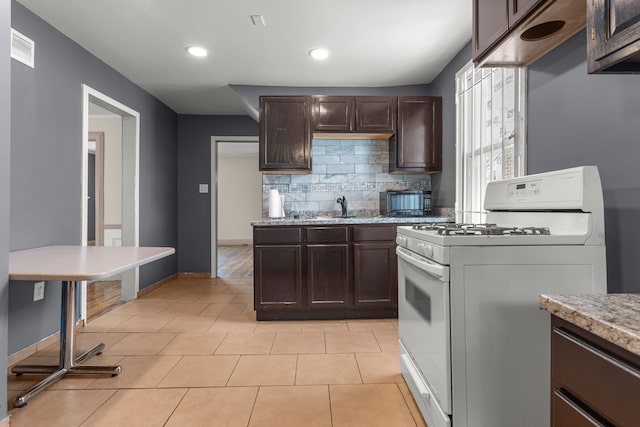 kitchen featuring white gas stove, dark brown cabinets, light countertops, and decorative backsplash